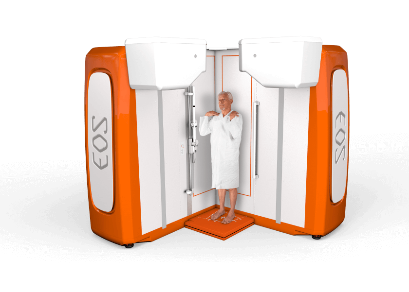 An adult patient stands on a specialized EOS imaging platform for a diagnostic procedure. The EOSedge system captures detailed diagnostic images of the patient's body.