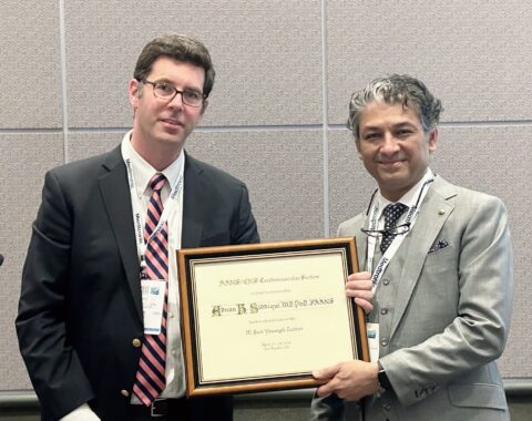 Dr. Siddiqui standing to the right of another man smiling and holding a framed award